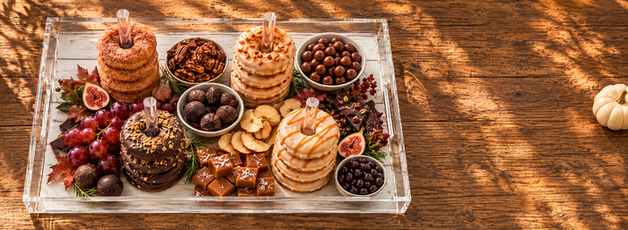 Fall dessert board with stacked donuts, caramels, figs and grapes on a clear acrylic tray on a rustic wood table