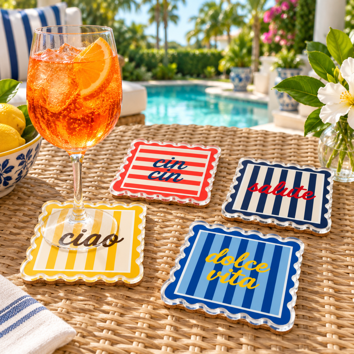 Striped acrylic coasters on a wicker table by a pool with an Aperol spritz