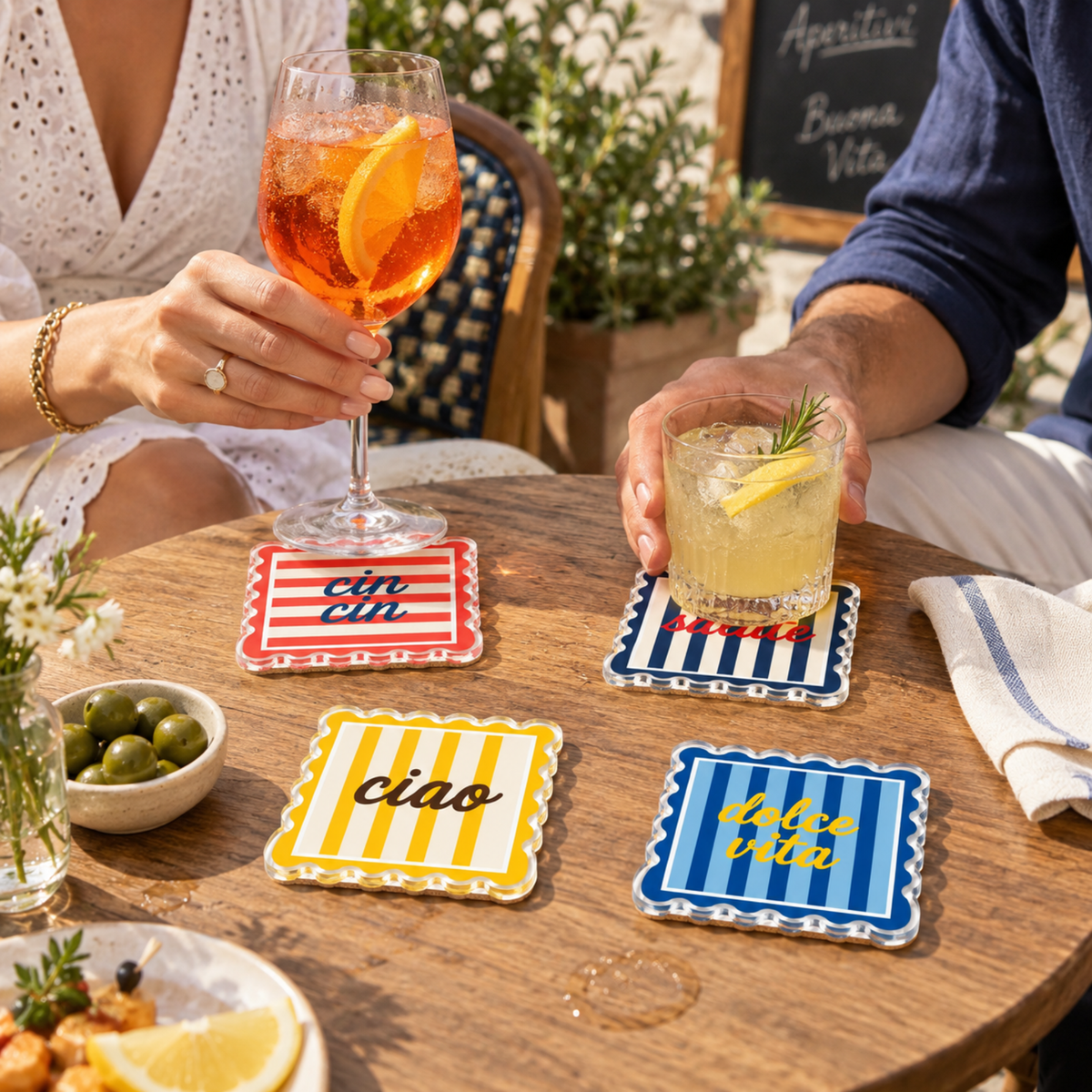 Guests holding spritz cocktails over the striped coasters on a wood table