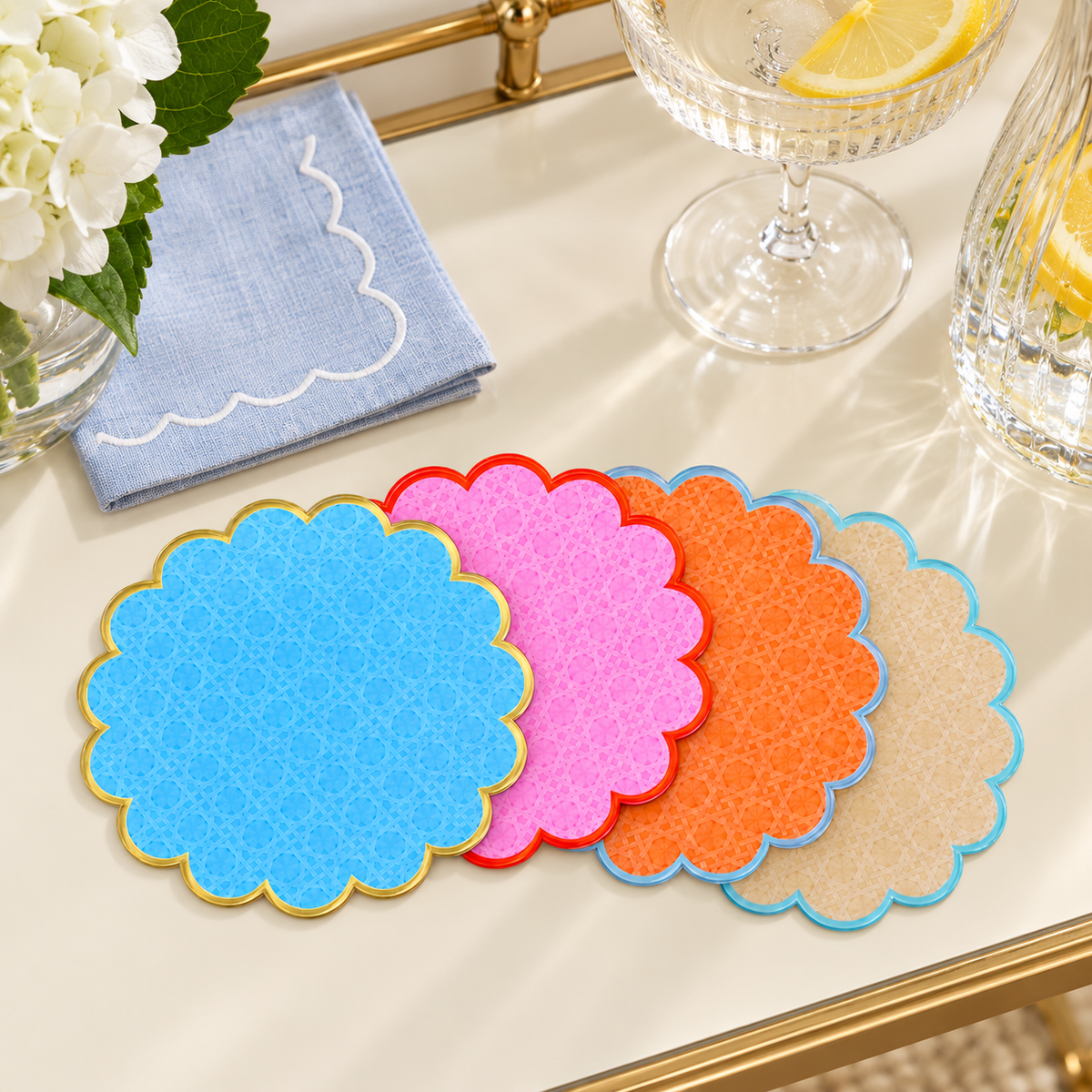 Stack of Cabana coasters on a brass bar cart beside a blue napkin and champagne glasses