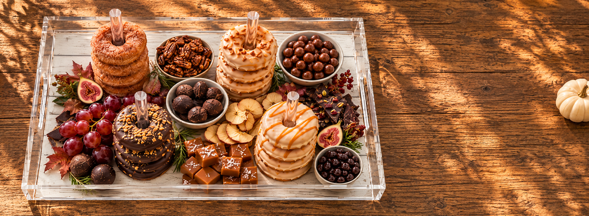 Fall dessert board with stacked donuts, caramels, figs and grapes on a clear acrylic tray on a rustic wood table