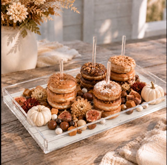 Fall donut board with glazed and chocolate donuts stacked on the dowels, figs, caramels and white pumpkins on a rustic porch table