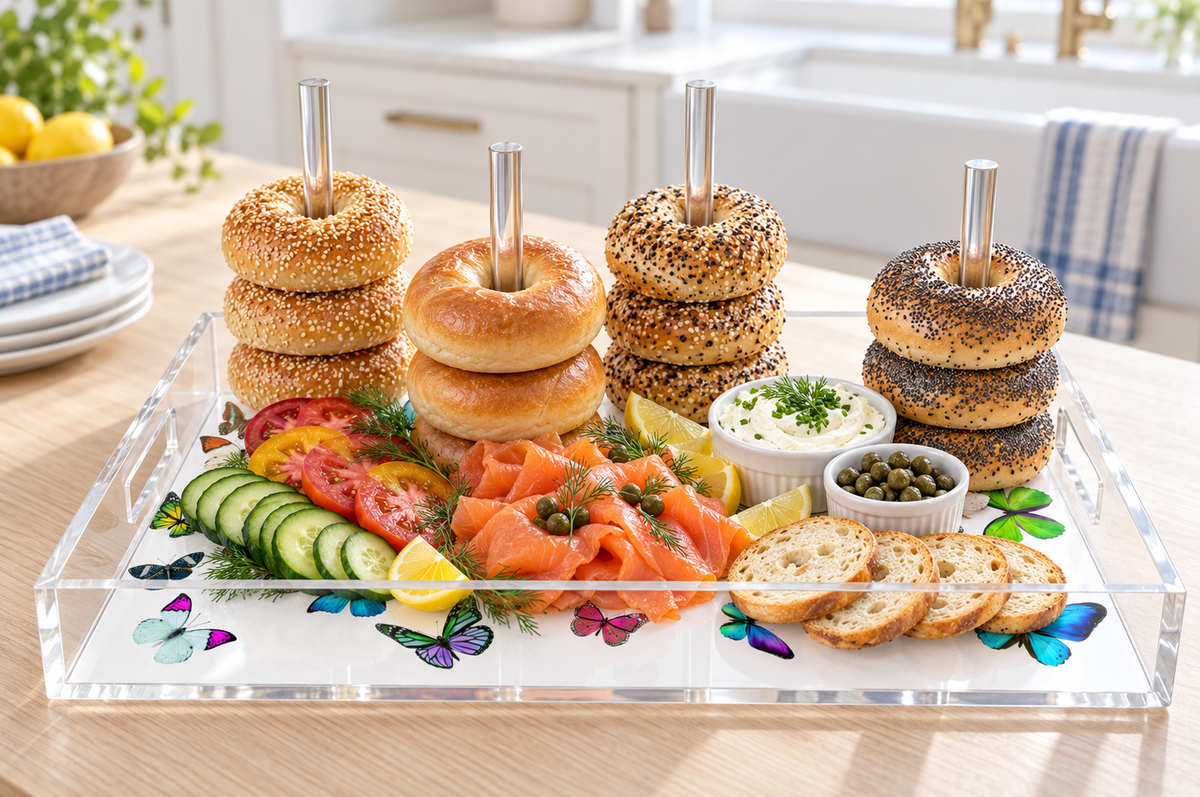 Bagels stacked on the clear acrylic dowels over a white butterfly print base with smoked salmon, cucumber, capers, cream cheese and toast in a sunny kitchen