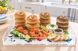 Bagels stacked on the clear acrylic dowels over a white butterfly print base with smoked salmon, cucumber, capers, cream cheese and toast in a sunny kitchen