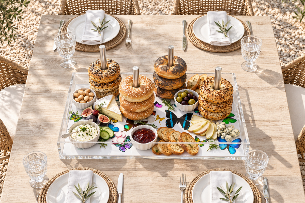 Butterfly bagel tray with bagel stacks, olives, cheese and dips at the center of an outdoor lunch table set for six