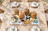 Butterfly bagel tray with bagel stacks, olives, cheese and dips at the center of an outdoor lunch table set for six