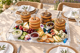 Bagels on the dowels with cheese, figs, radishes and olives on a patio table set with woven chargers
