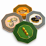 Four octagonal striped coasters fanned out: green with skewered olives, pink with oysters, orange with a sardine tin and white with caviar