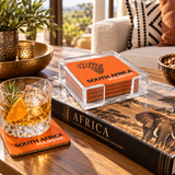 South Africa Bon Voyage acrylic coaster under a cocktail glass, with the rest of the set in its acrylic holder on a coffee table