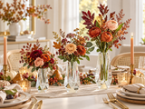 Three clear acrylic bud vases with rust and burgundy fall flowers, pumpkins and taper candles