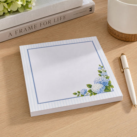 Hydrangea notepad on a wood desk with a cream pen and coffee mug