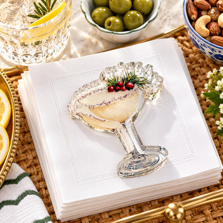 Festive Cocktail acrylic napkin weight, a coupe with cranberries and rosemary, on white cocktail napkins on a rattan tray with olives and nuts