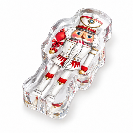 Nutcracker acrylic napkin weight on a white background: a nutcracker soldier in red and white with gold trim, set in clear acrylic