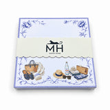 Proper Beach Club 5x5 notepad wrapped in its scalloped MH band, with a lavender border, blue florals and a straw tote