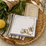 Proper Pantry notepad in a woven basket with fresh herbs, a lemon and a market list