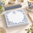 Hamsa and Ahava 5x5 notepad on a desk with a gold pen, blue-and-white teacup, books and white flowers