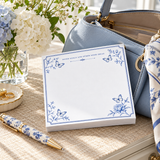 Notes and Goals notepad on a woven table with a blue handbag, white hydrangeas and a blue-and-white pen