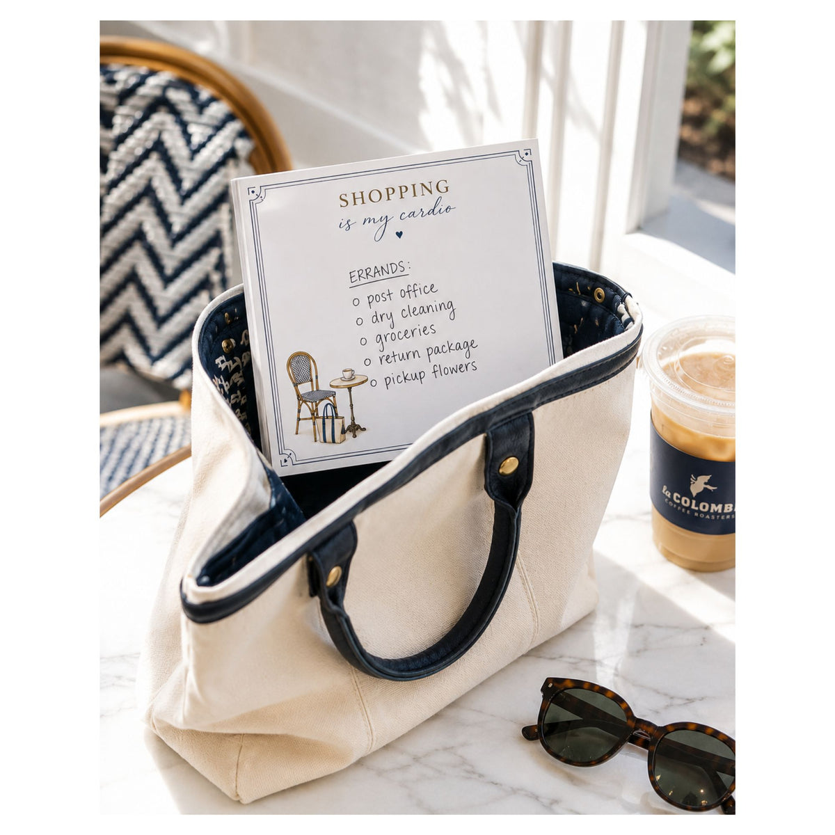 Shopping Is My Cardio 5x5 notepad with a handwritten errands list in a canvas tote on a marble cafe table with sunglasses